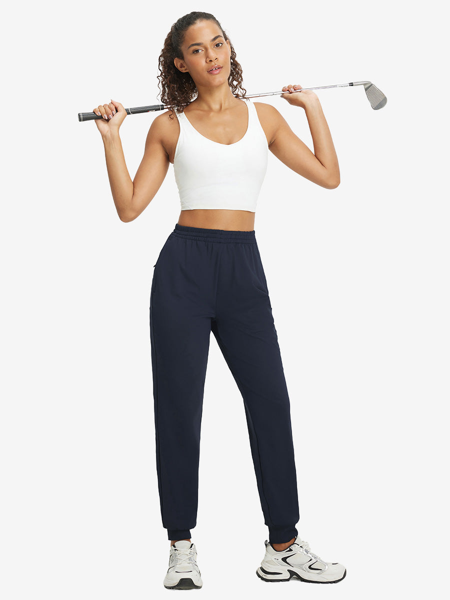 Model holding golf club behind neck while wearing lightweight women's stretchy joggers sweatpants in navy.