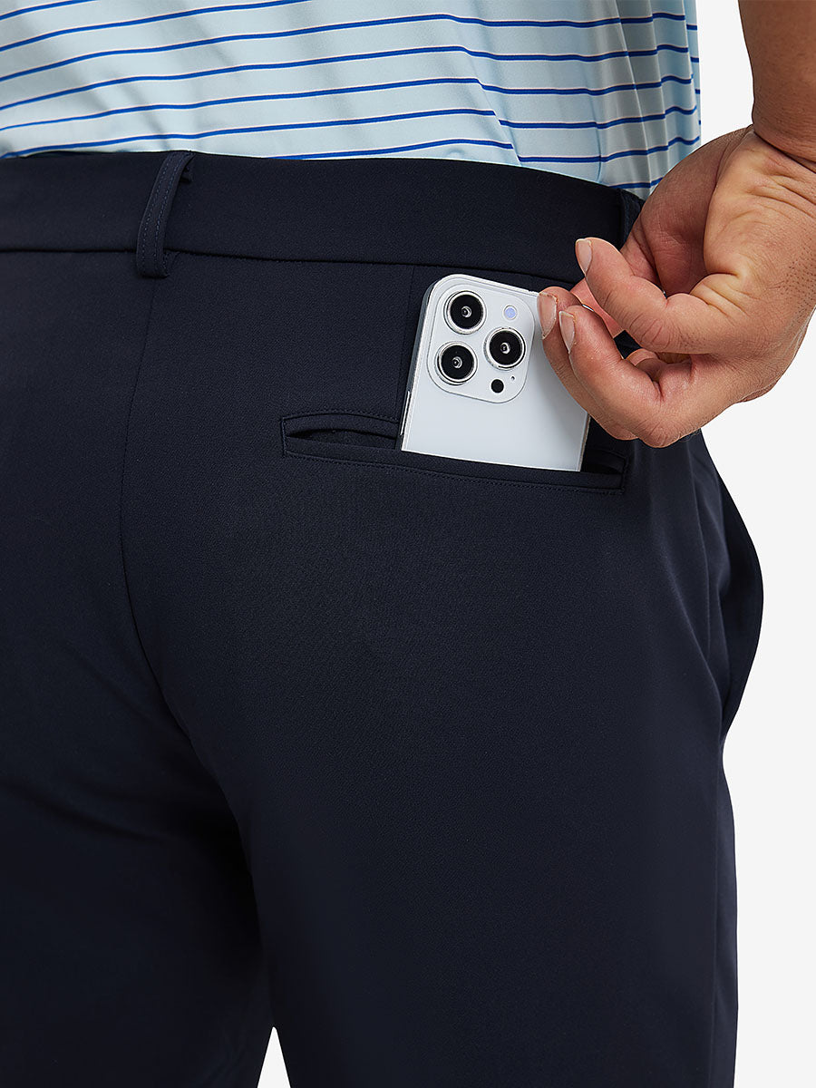 Back view of model putting phone into pocket while wearing lightweight moisture wicking dress pants in navy.