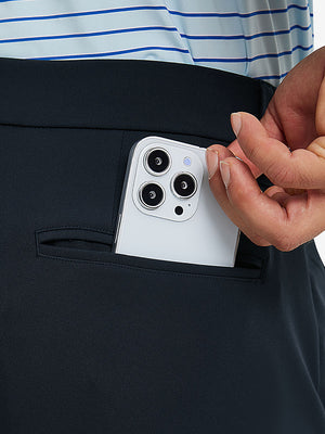 Close detail of hand placing phone into back pocket of lightweight moisture wicking dress pants in navy.