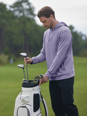 Model placing golf club into bag wearing classic heather pullover hoodies with 2 pocket in light purple melange