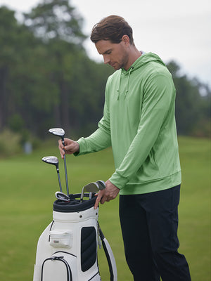 Model placing golf club into bag wearing classic heather pullover hoodies with 2 pocket in light green melange
